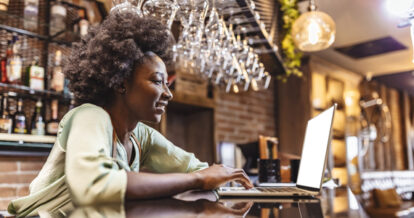 Woman working on a laptop in front of a bar.
